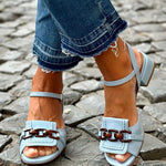 Light blue sandals with double buckle strap and low block heel on cobblestones