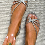Metallic silver strappy flat sandals with bow-like accent at toe