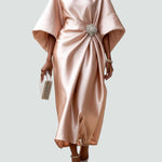 Beige satin long evening dress with draped batwing sleeves and jeweled waist brooch.