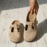 Beige suede slide clogs with square buckle strap and cutout instep, shown up close
