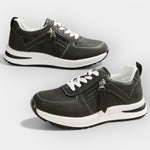 Anatomical black sneakers with white laces, side zipper, and white rubber sole.