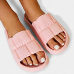 Light pink slide sandals on feet, padded straps and open-toe slide design