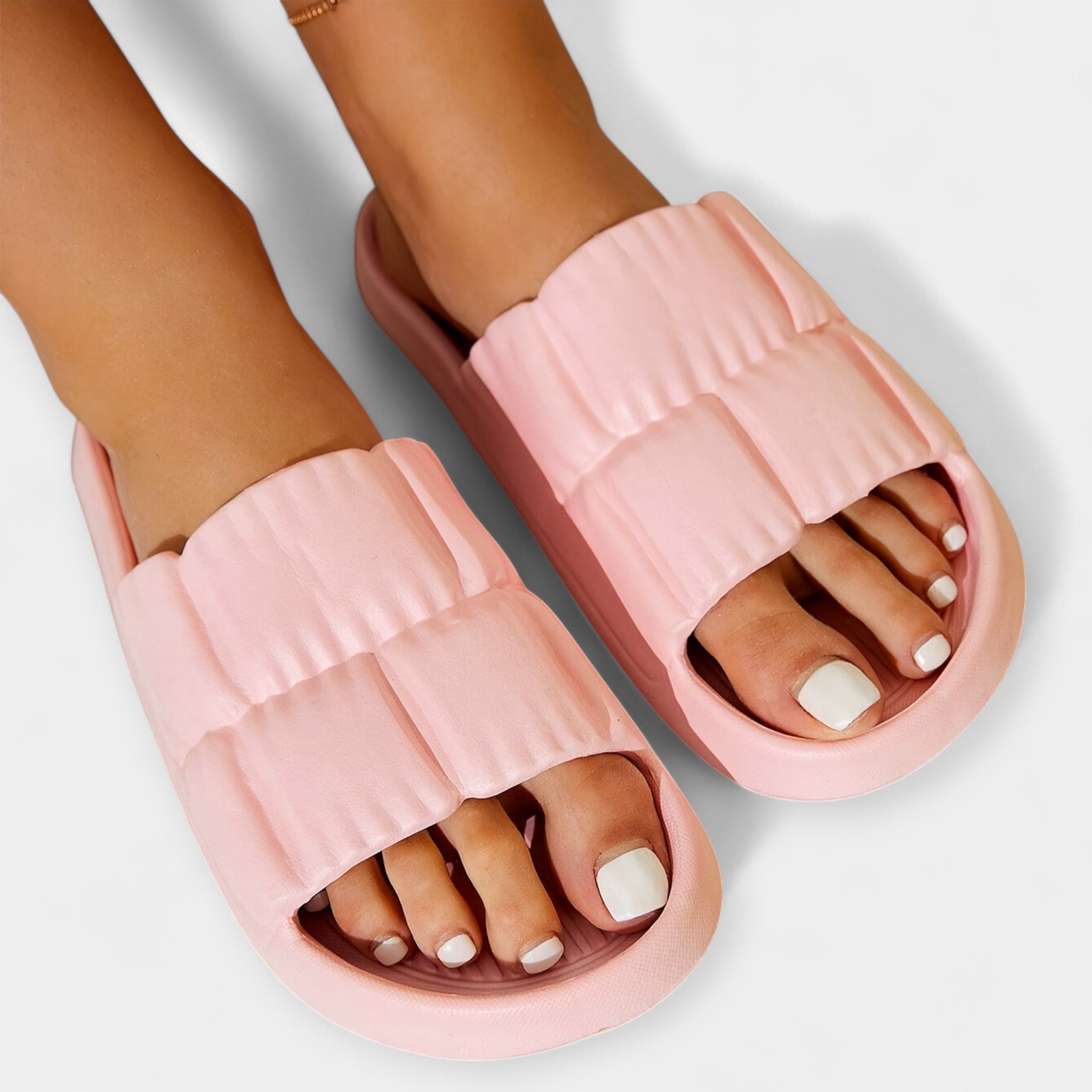 Light pink slide sandals on feet, padded straps and open-toe slide design