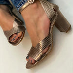 Metallic bronze heeled sandals with crisscross straps and buckle ankle strap.