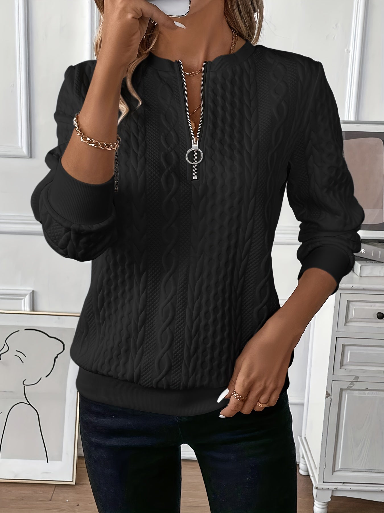 Black cable-knit zip-front sweater with half zipper and long sleeves, textured braid pattern.