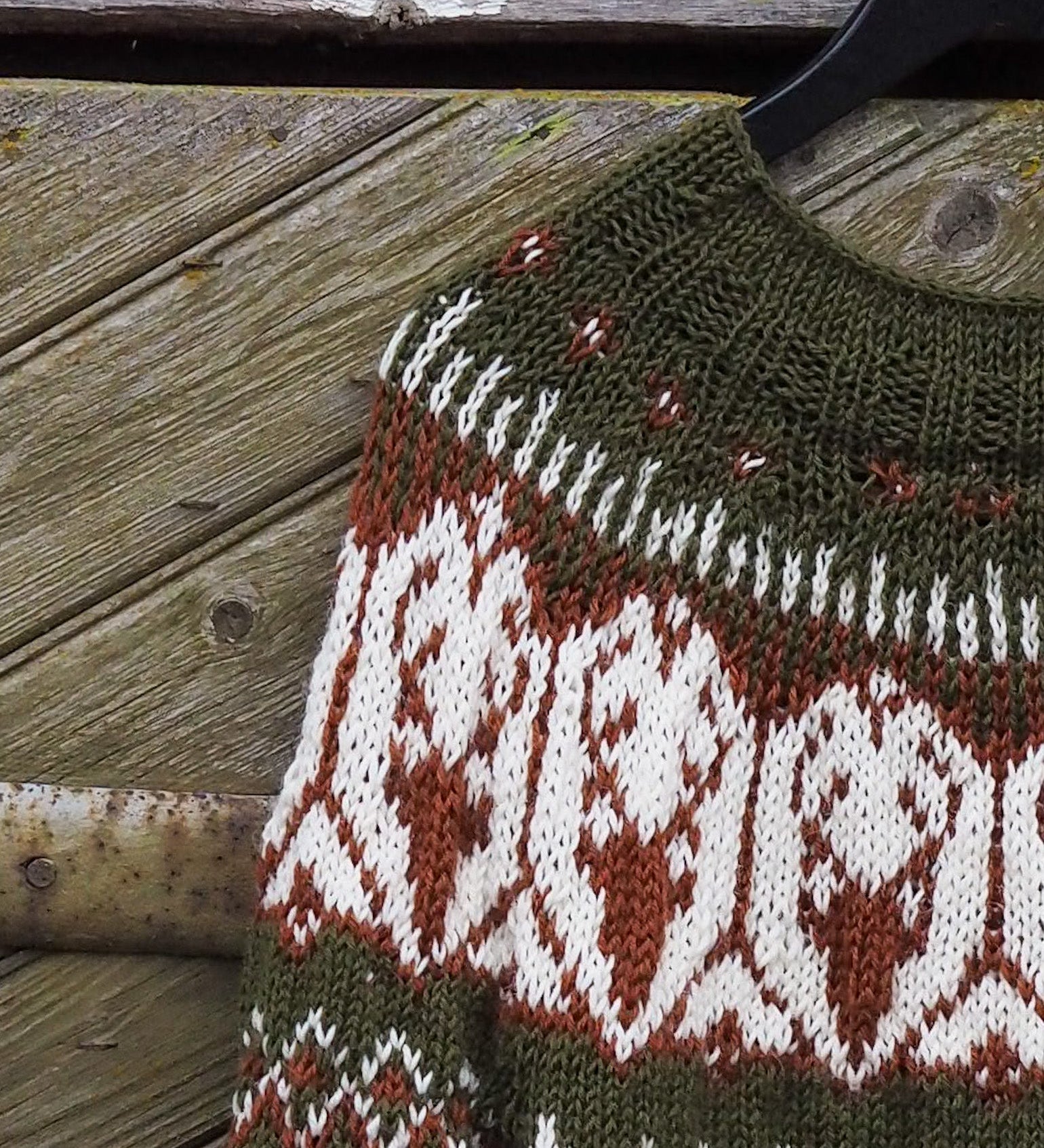 Olive green knit sweater close-up with white and red geometric diamond pattern