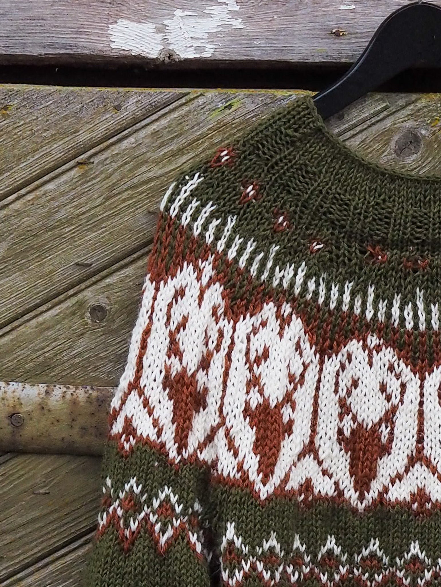 Olive green knit sweater close-up with white and red geometric diamond pattern