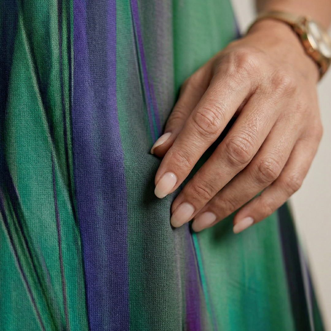 Close-up of green and purple vertical-striped fabric with soft sheen, hand on dress