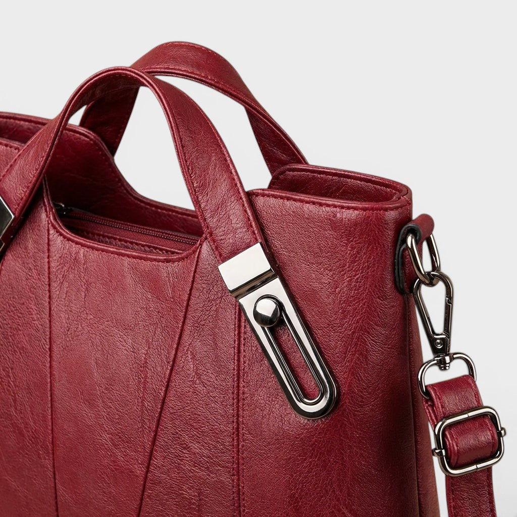 Burgundy leather handbag close-up of top handle hardware and front panel seams