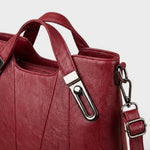 Burgundy leather handbag close-up of top handle hardware and front panel seams