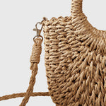 Close-up of woven straw bag with metal clasp, braided strap and decorative tassel.