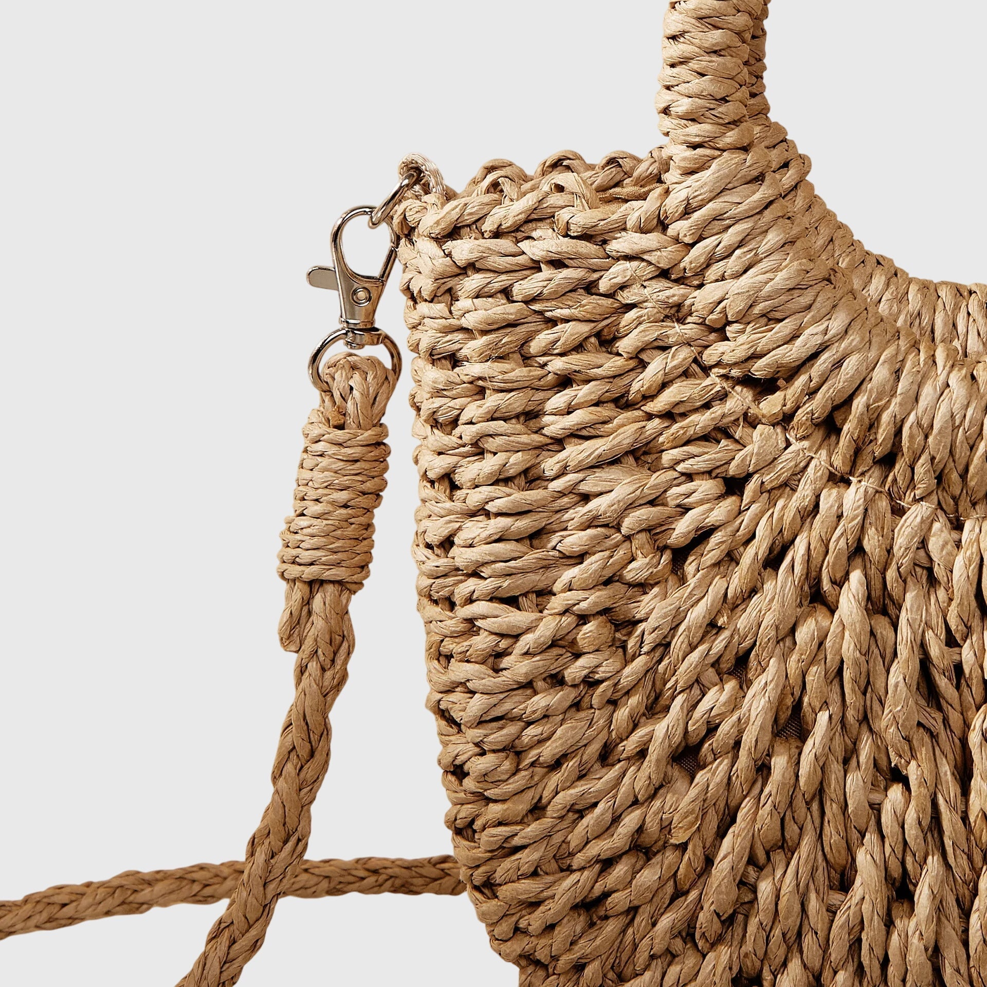 Close-up of woven straw bag with metal clasp, braided strap and decorative tassel.