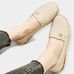 Beige slip-on loafers showing floral emblem at the heel and stitched apron toe