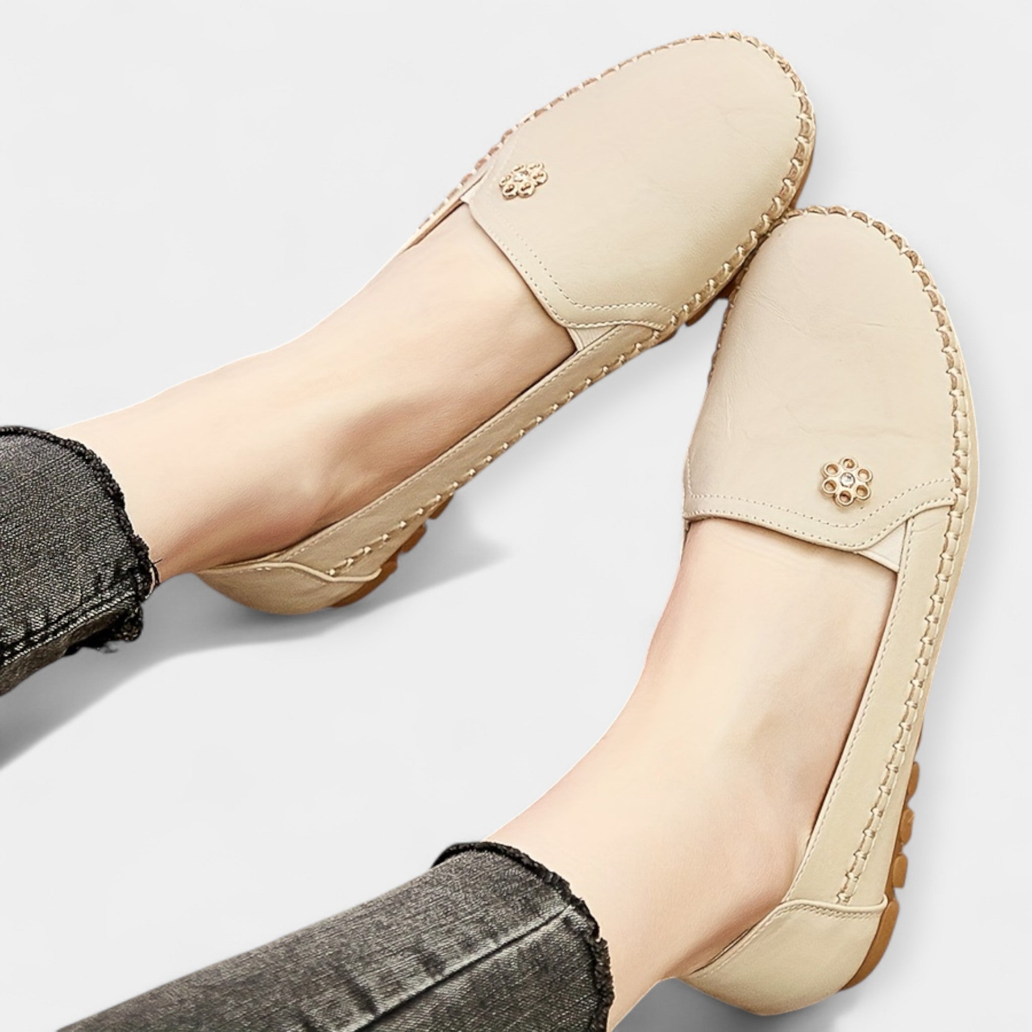 Beige slip-on loafers showing floral emblem at the heel and stitched apron toe
