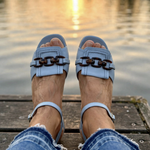 Light blue double-buckle sandals with block heel on feet by the water