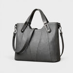 Gray leather handbag with top handles, metal buckles, and adjustable shoulder strap