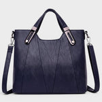 Navy leather handbag with top handles, metal buckles, and crossbody shoulder strap