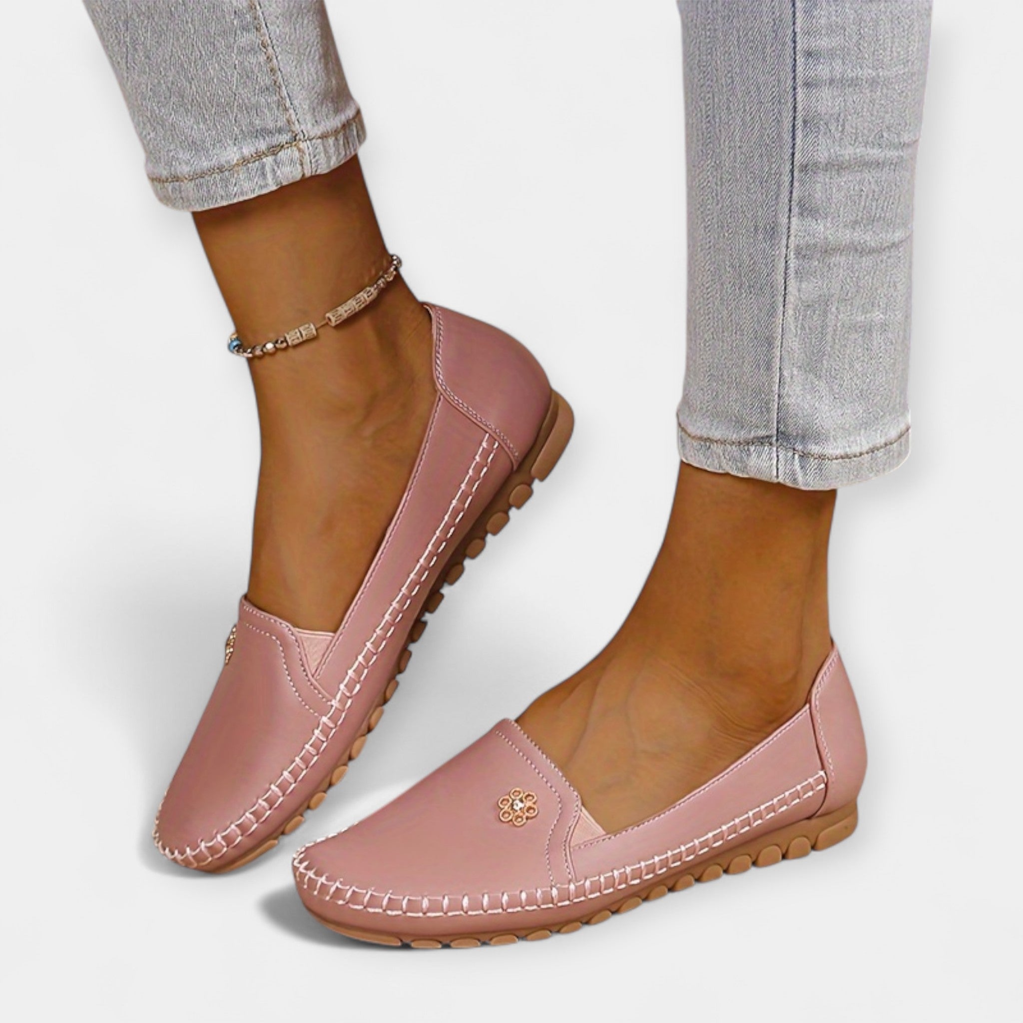 Blush pink slip-on loafers with soft sole, stitched edges, and floral emblem on upper