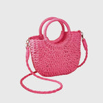 Hot pink woven straw shoulder bag with ring handles and long crossbody strap.