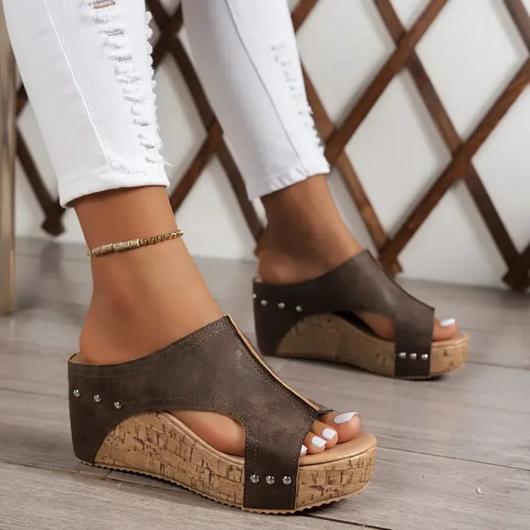 Brown heeled wedge sandal with open toe, studded cross strap and cork sole