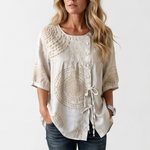 Off-white vintage blouse with round neckline, button placket, circular embroidery, and tassel trim