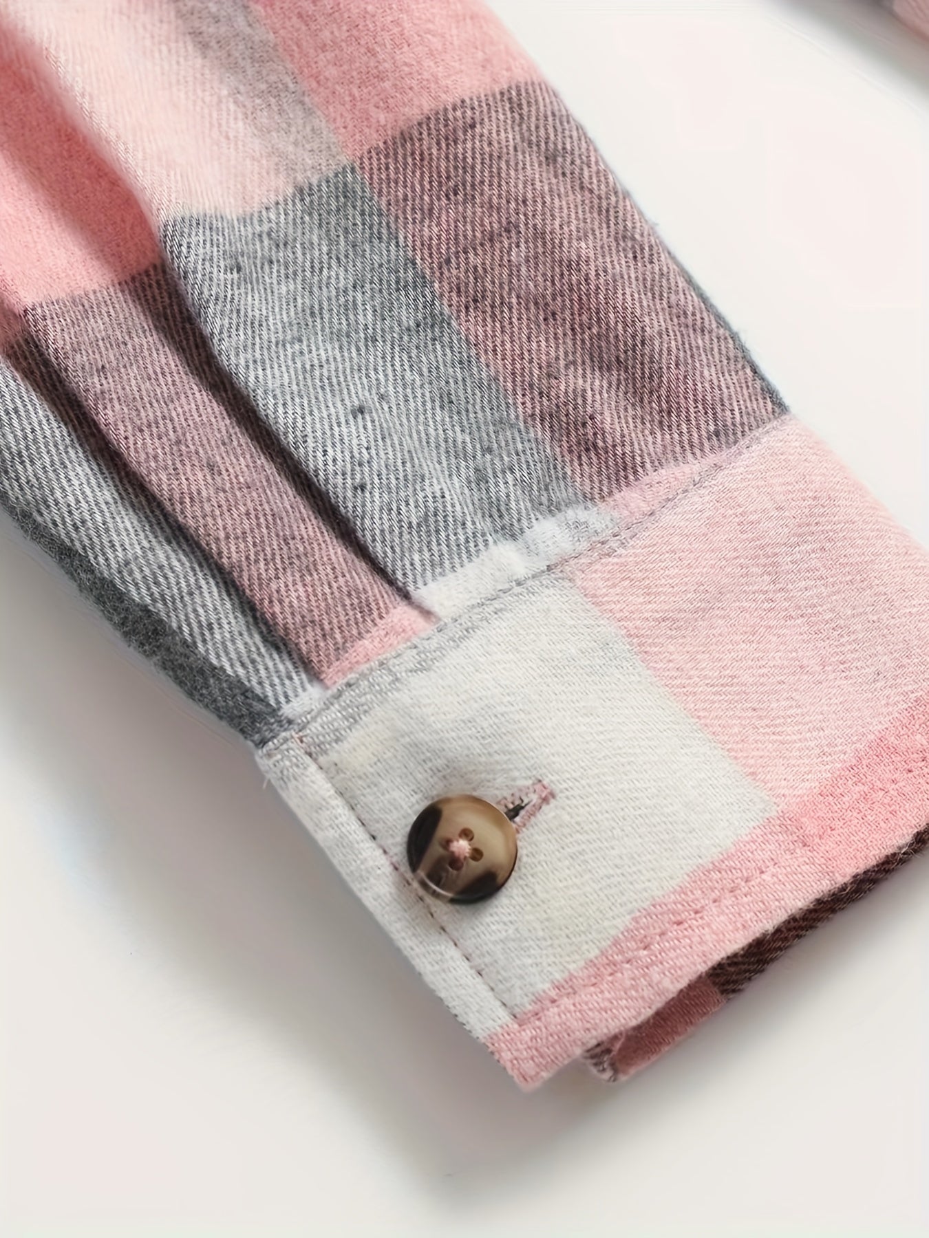 Plaid shirt cuff with brown button and pink, gray, and white check pattern