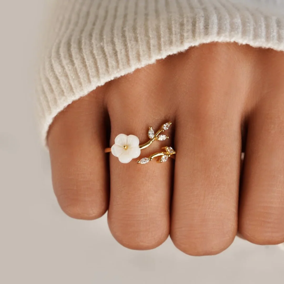 Gold-tone ring with white flower and clear marquise crystals worn on fingertip