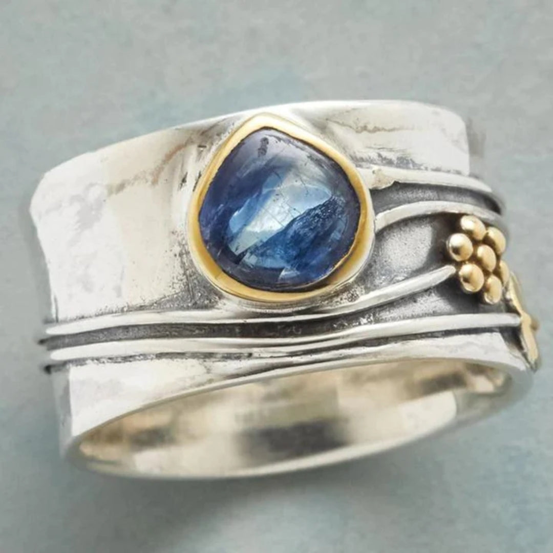Silver-tone ring with oval blue gemstone bezel and gold-tone bead side accents