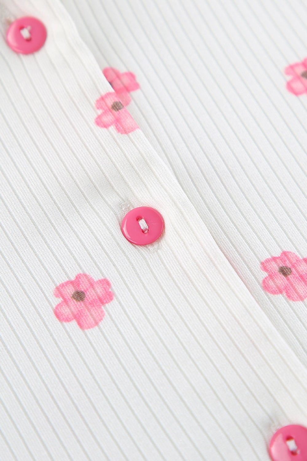Close-up of white pajama top fabric with pink flower print and pink button placket.