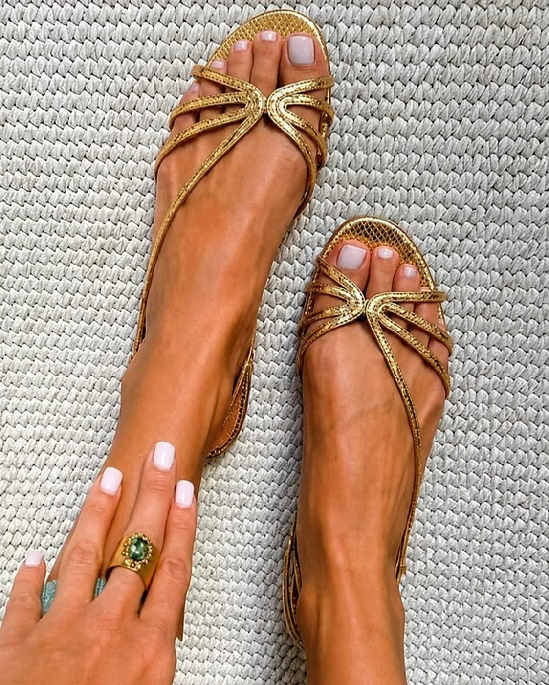 Metallic gold strappy flat sandals with bow-style metal ornament at toe