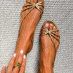 Metallic gold strappy flat sandals with bow-style metal ornament at toe