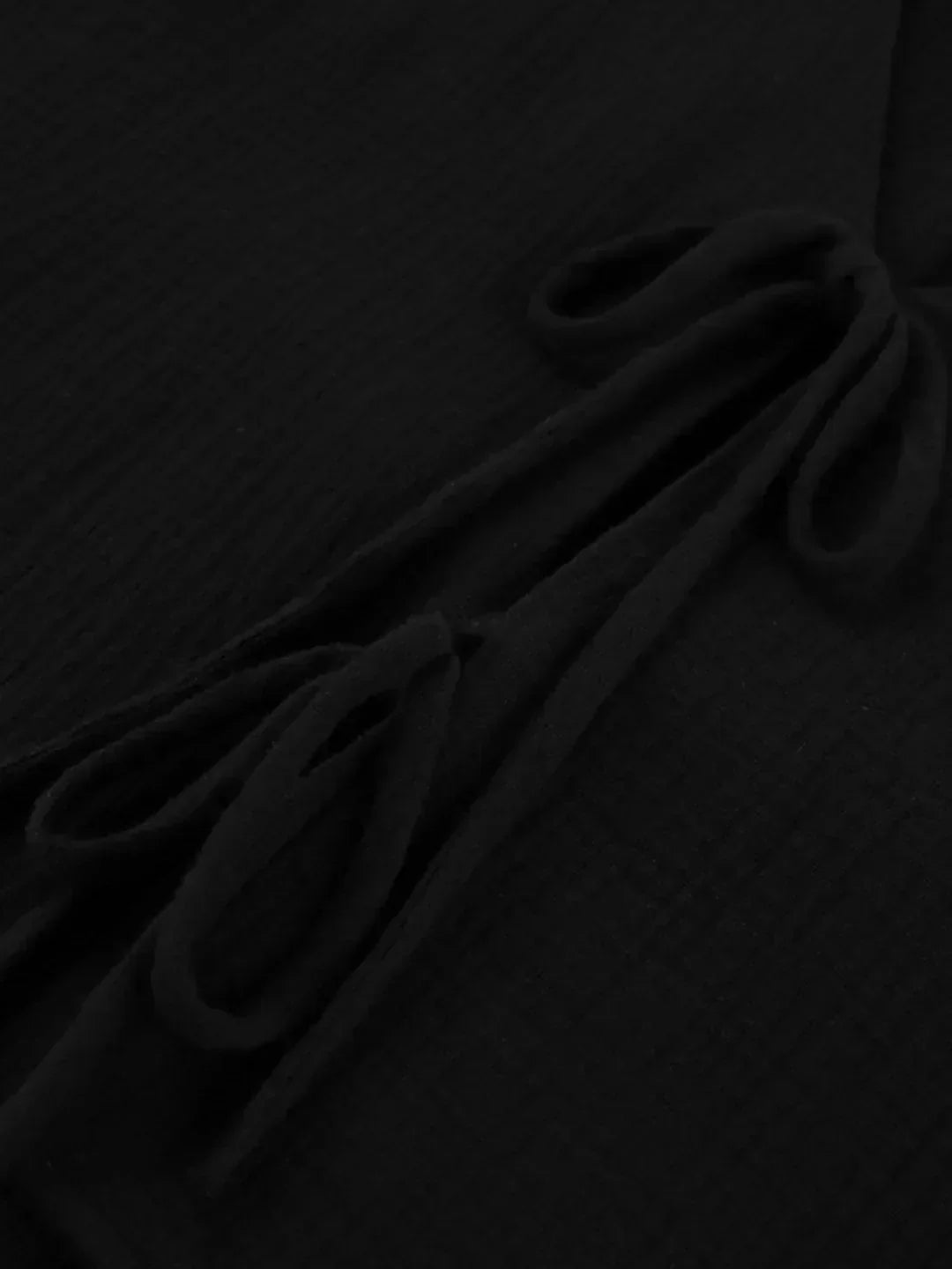 Close-up of black textured fabric with gathered folds and tie details