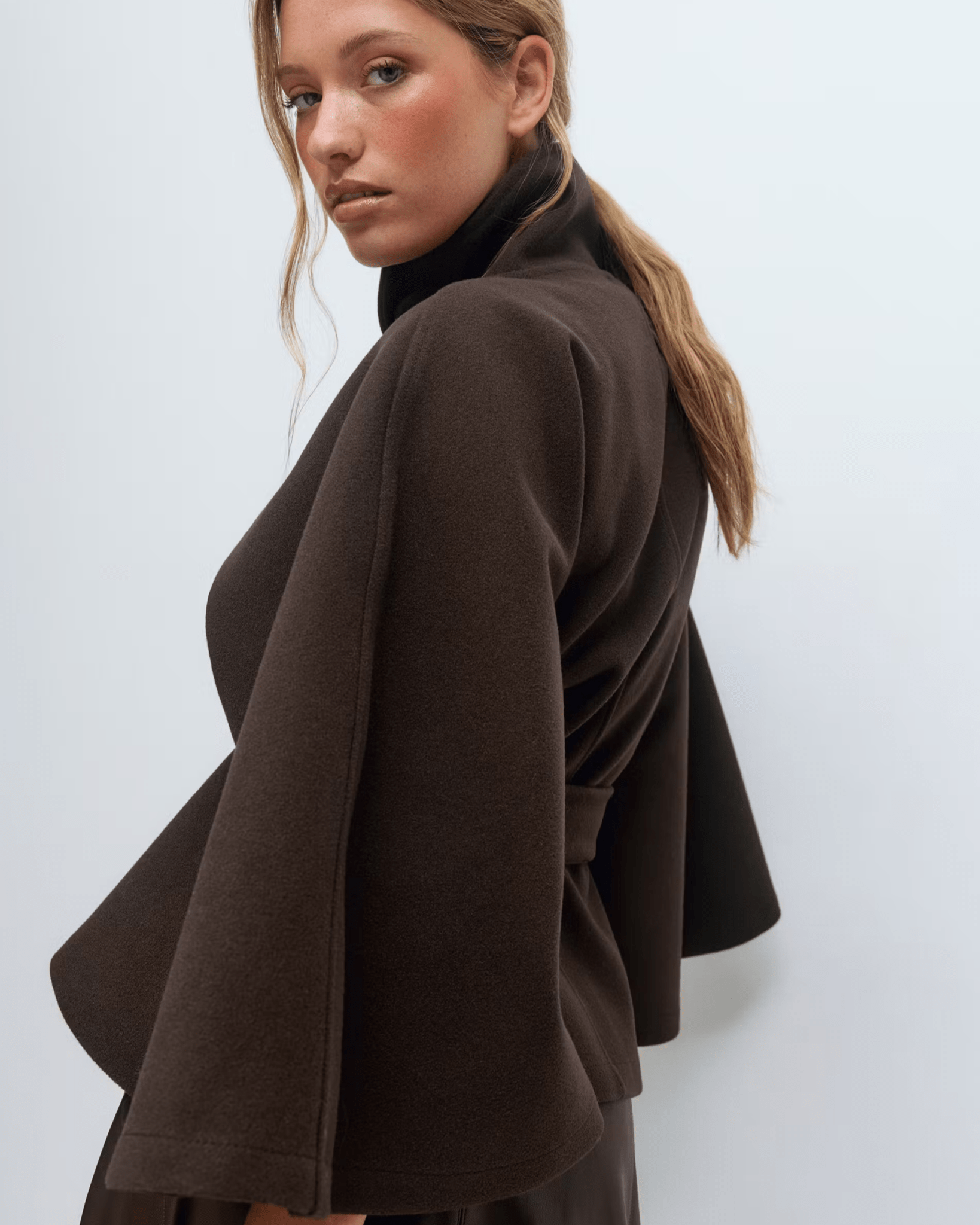 Dark brown belted jacket with high collar and button front, cape sleeves