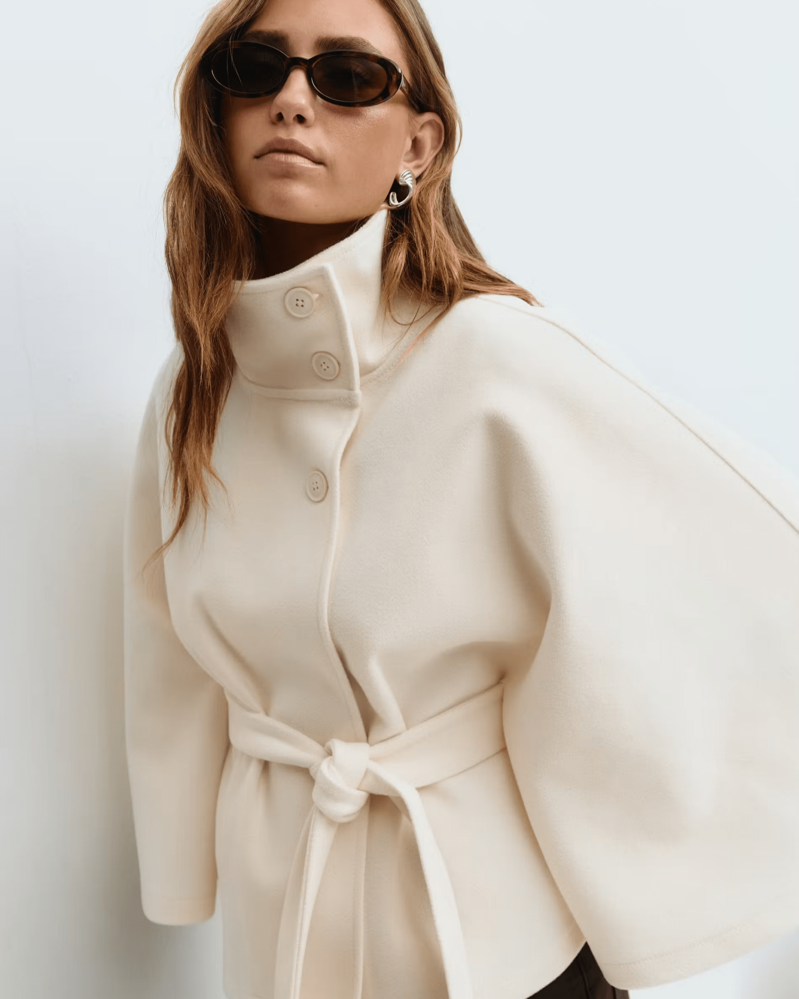 Cream belted jacket with high neck, button front, cape sleeves