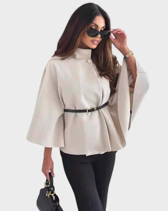 Light beige cape-style coat with high neck, button closure, and waist belt