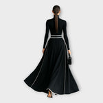 Black long-sleeve maxi dress with high back, silver-buckle belt, flowing skirt with piping