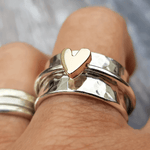 Silver heart-ring with gold heart centerpiece, shown on finger with stacked rings