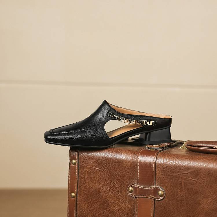 Black leather mule with cutout instep strap and patterned heel, on a brown bag.