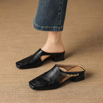 Black leather mule flats with square toe and low block heel, worn with jeans.