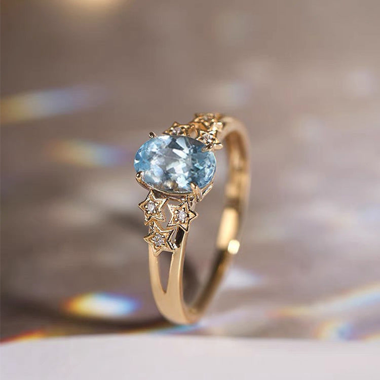 Gold-tone ring with oval blue gemstone and star-like crystal accents