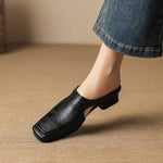 Black leather mule with cutout instep strap and low block heel on bare foot.
