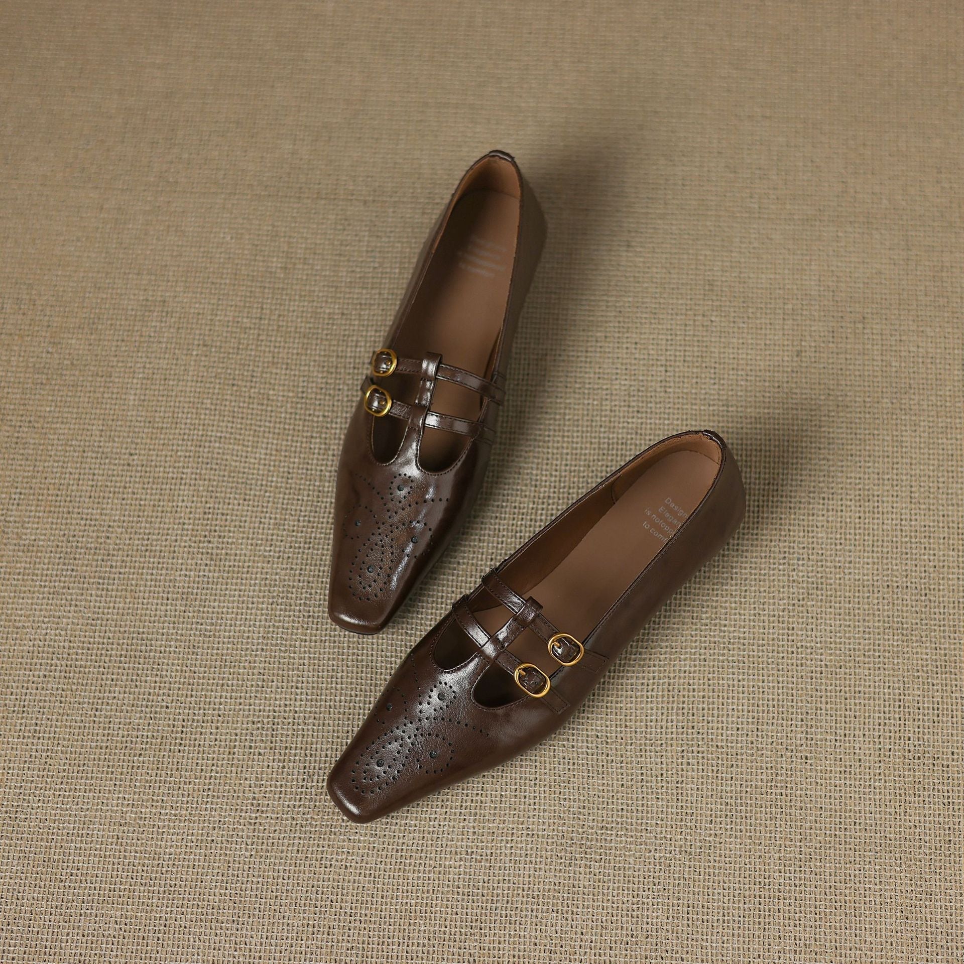 Brown Mary Jane flats pair on textured surface, perforated toe and two buckles