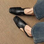 Black leather mules with square toe and open instep strap, close-up on legs.