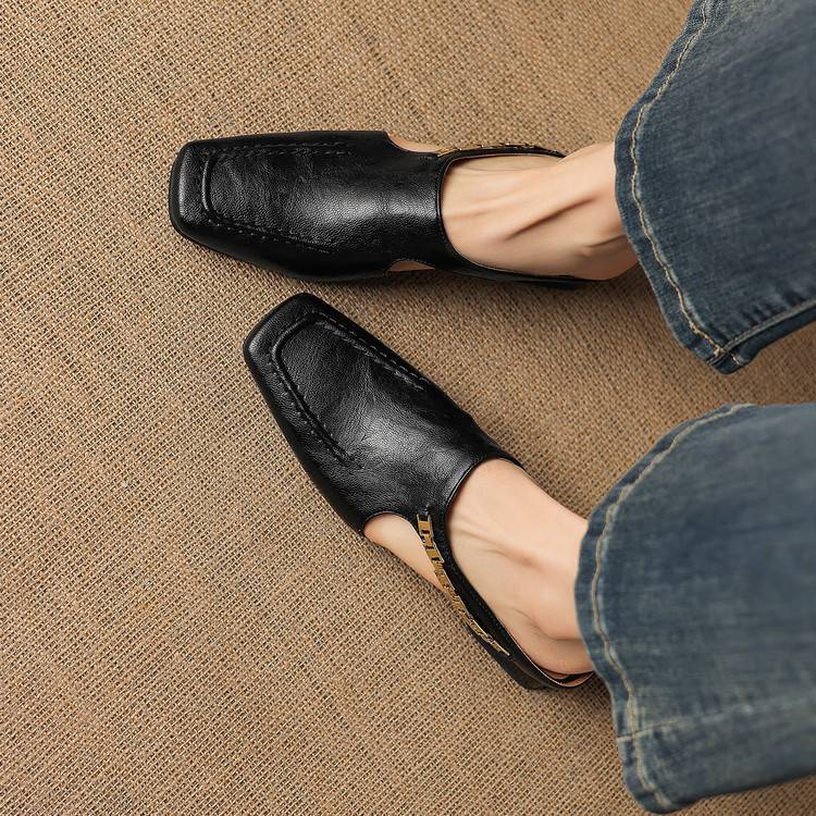 Black leather mules with square toe and open instep strap, close-up on legs.