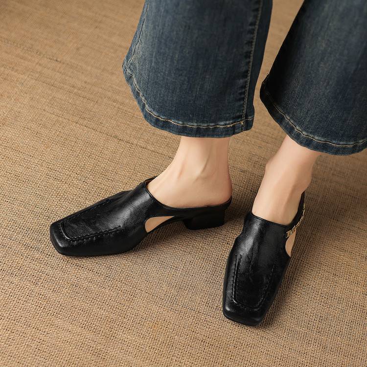 Pair of black leather mules with square toe and low heels on a beige fabric surface.