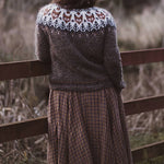 Fair isle knit pullover with crew neck and long sleeves, worn over plaid skirt.