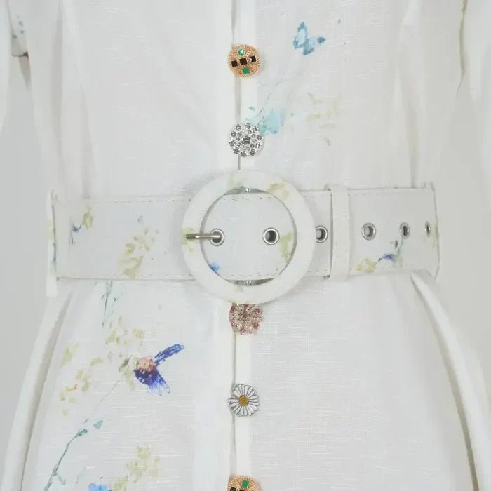 Waistband and button detail with decorative charms on a white-blue floral dress