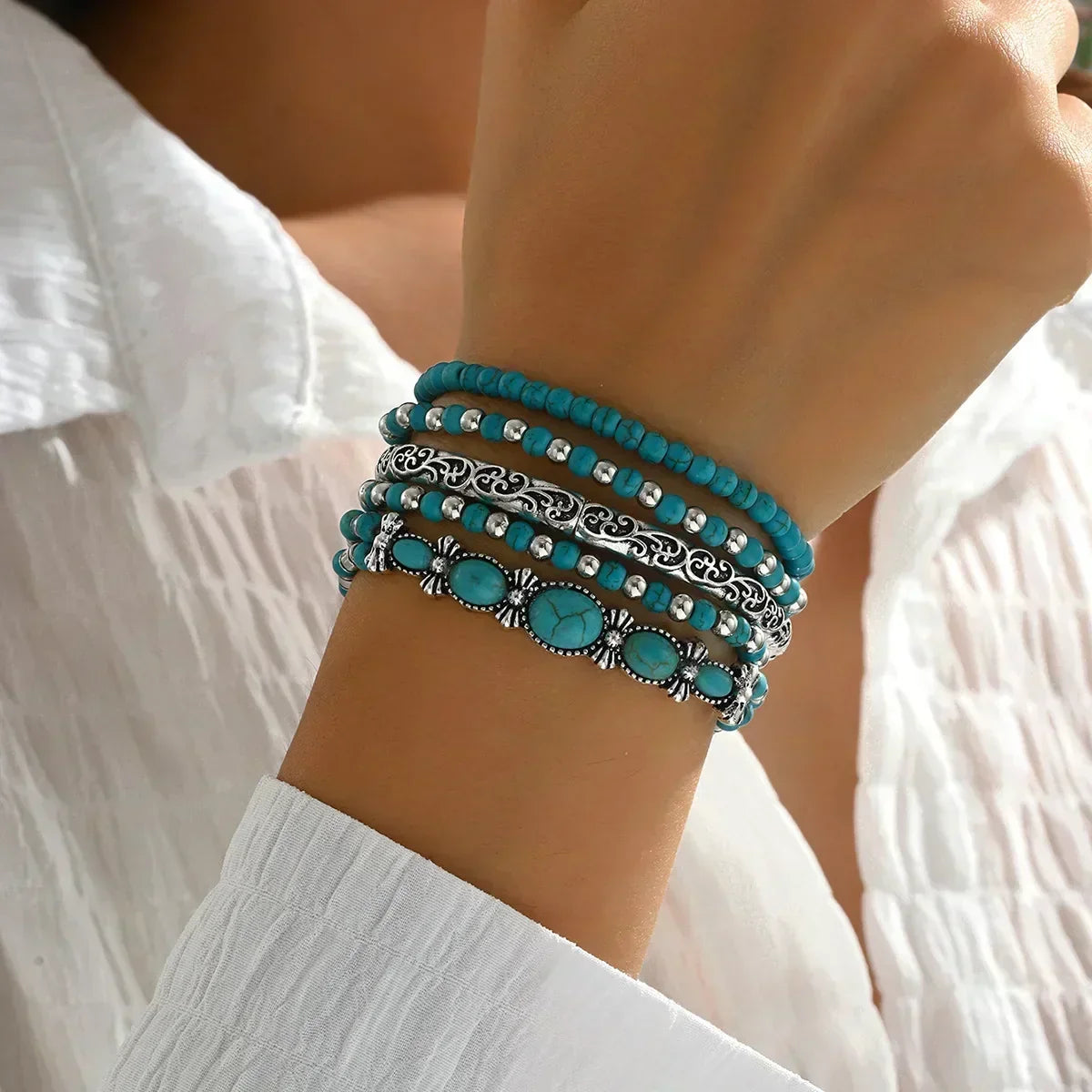 Turquoise beaded bracelets with silver filigree and oval charms worn on wrist
