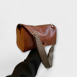 Medium brown crossbody bag with woven strap and top zip, structured rounded shape.