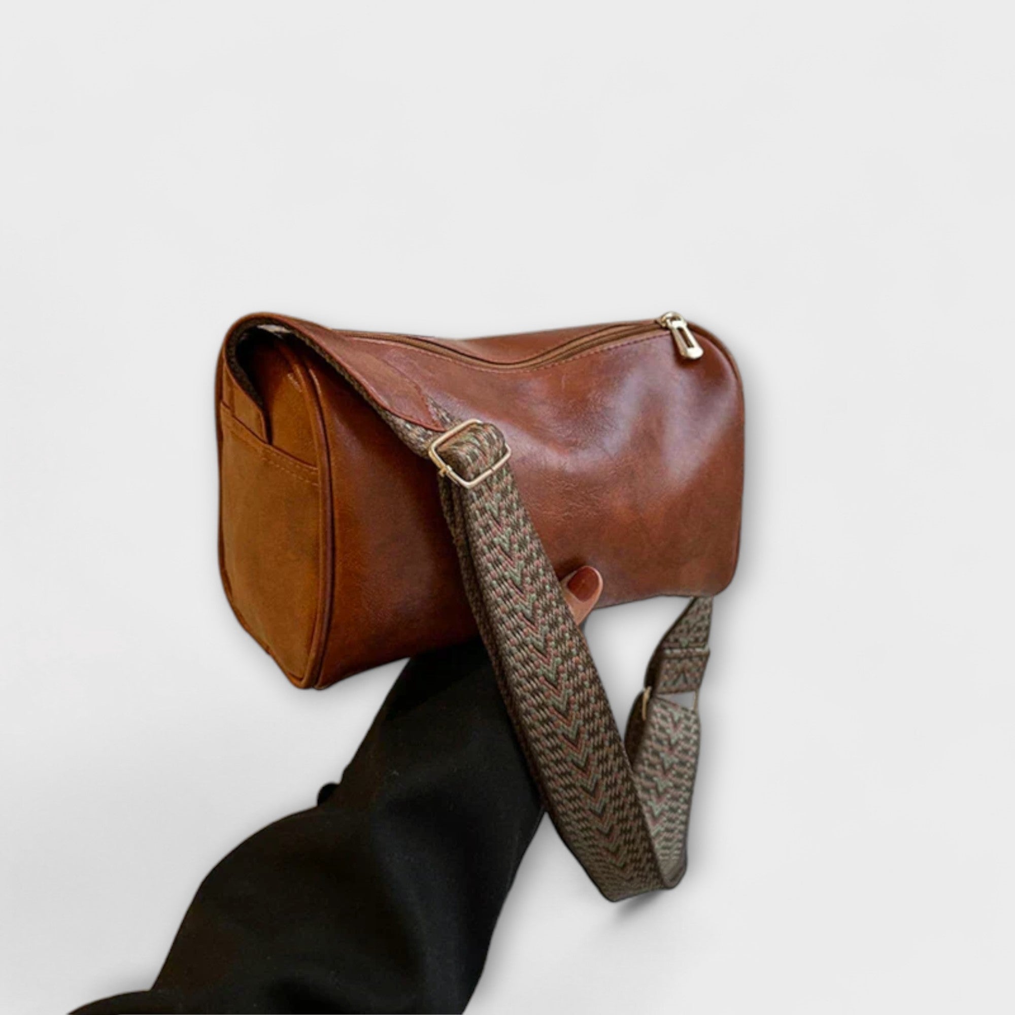 Medium brown crossbody bag with woven strap and top zip, structured rounded shape.